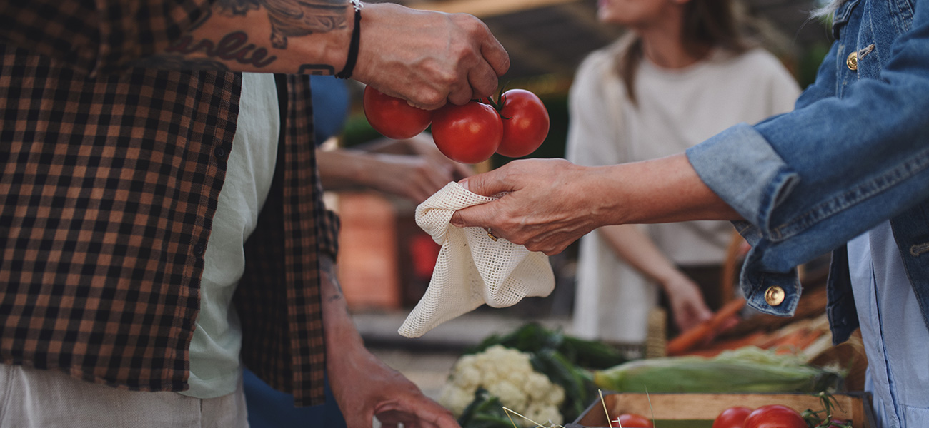 Person buying locally grown produce at an open-air market.