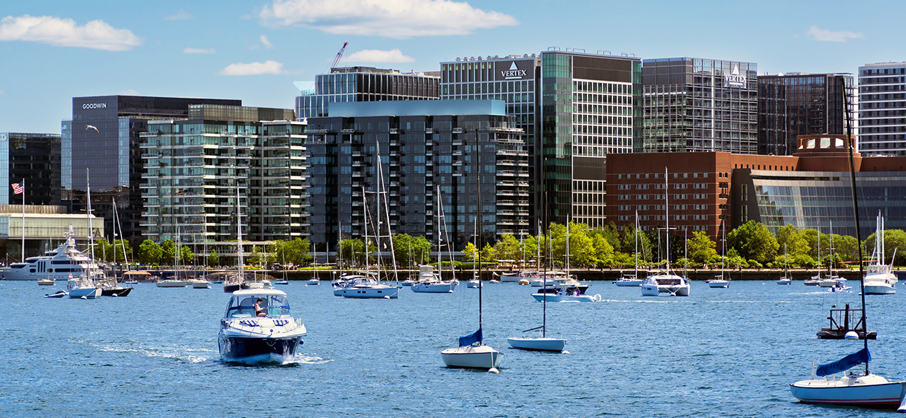 Boats in the water of the Boston Harbor with the Seaport District in the background.